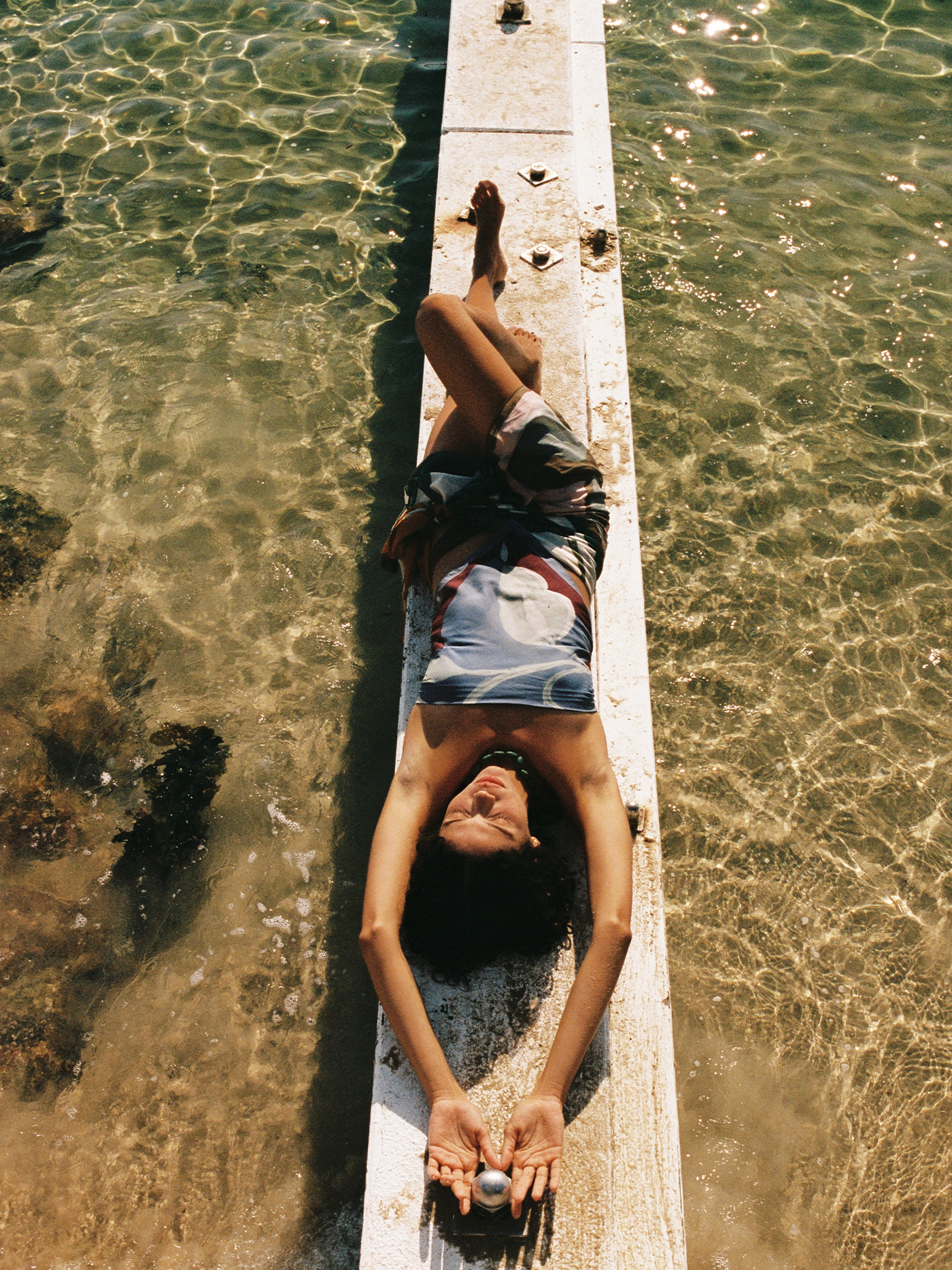 Person lying on a wooden pier over clear water